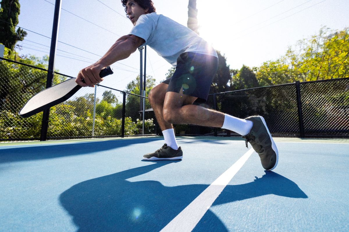 Person playing pickleball on an outdoor court with trees in the background. Tru Stride Co bringing Xero Shoes to Canada