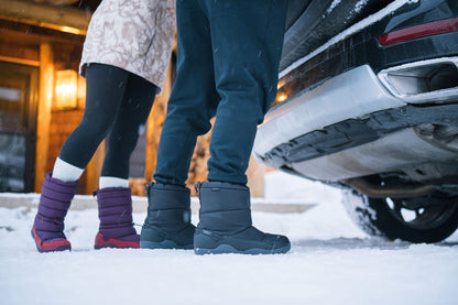 Two people wearing winter boots in the snow next to a car.  Tru Stride Co brings Xero shoes to Canada