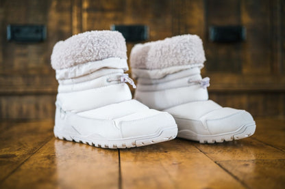 Pair of white winter boots with fluffy tops on a wooden floor.  Tru Stride Co brings Xero shoes to Canada