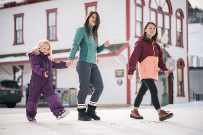 Three people walking on a snowy street in front of a building with a red roof.  Tru Stride Co brings Xero shoes to Canada
